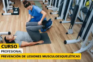 Terapeuta en uniforme azul ayudando a un paciente en el suelo del gimnasio a realizar un ejercicio de estiramiento con equipo de rehabilitación. Imagen promocional del curso de prevención de lesiones musculoesqueléticas.