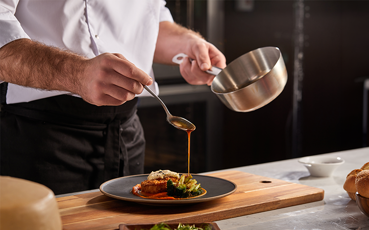Un cocinero echando salsa en un plato