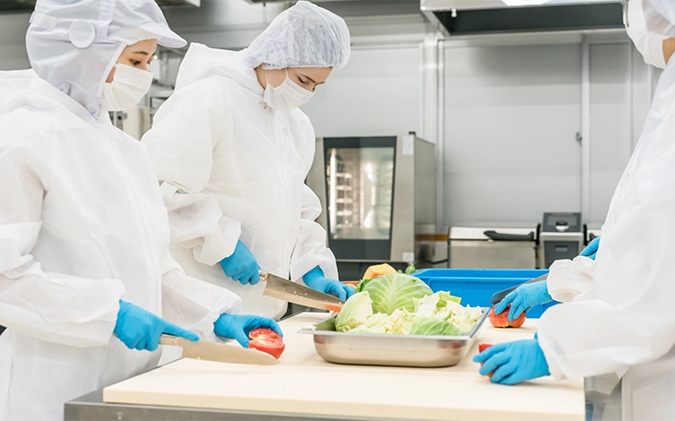 personal manipulando alimentos en una cocina industrial, aplicando normas de higiene, seguridad alimentaria y prevención de la contaminación durante la preparación de alimentos.
